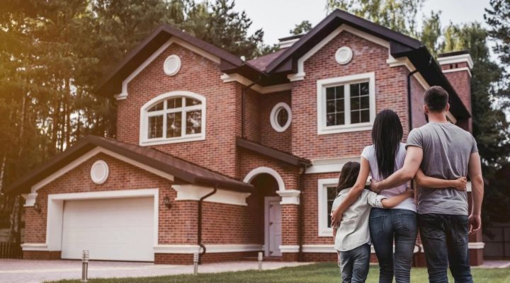 Family of three standing on street looking at house