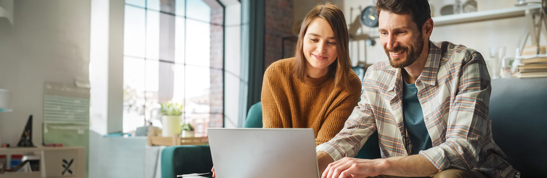 Couple going through finances on laptop while sitting on a couch in studio apartment